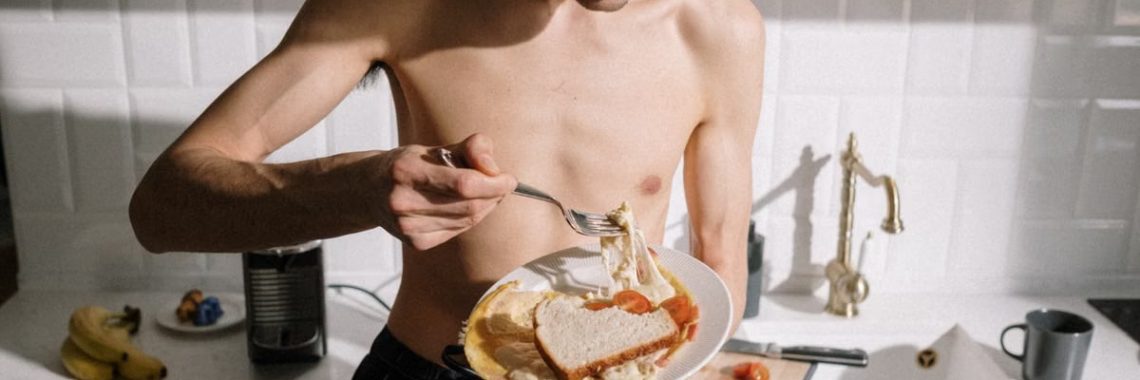 Young man eating breakfast in cozy, sunlit kitchen, enjoying a sandwich.