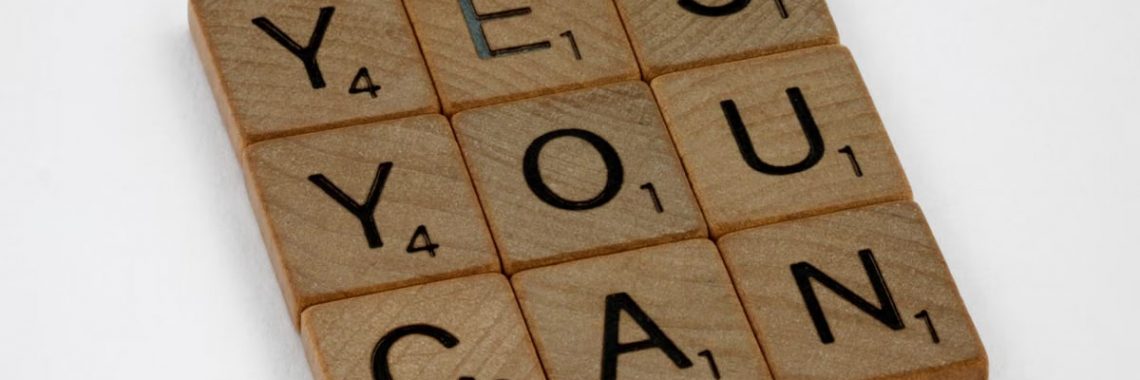 Wooden Scrabble tiles on white surface spelling 'Yes You Can,' promoting positivity and motivation.
